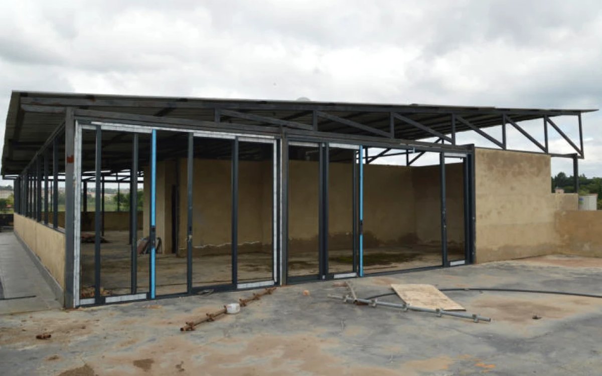Steel roof structure with trusses, columns and purlins over a single-storey building nearing completion.